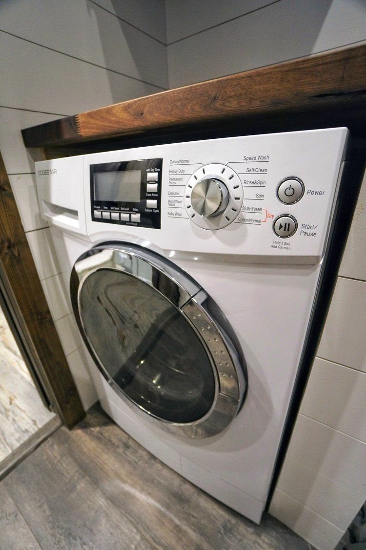 White washer-dryer combo machine installed under a wooden counter in a laundry room.