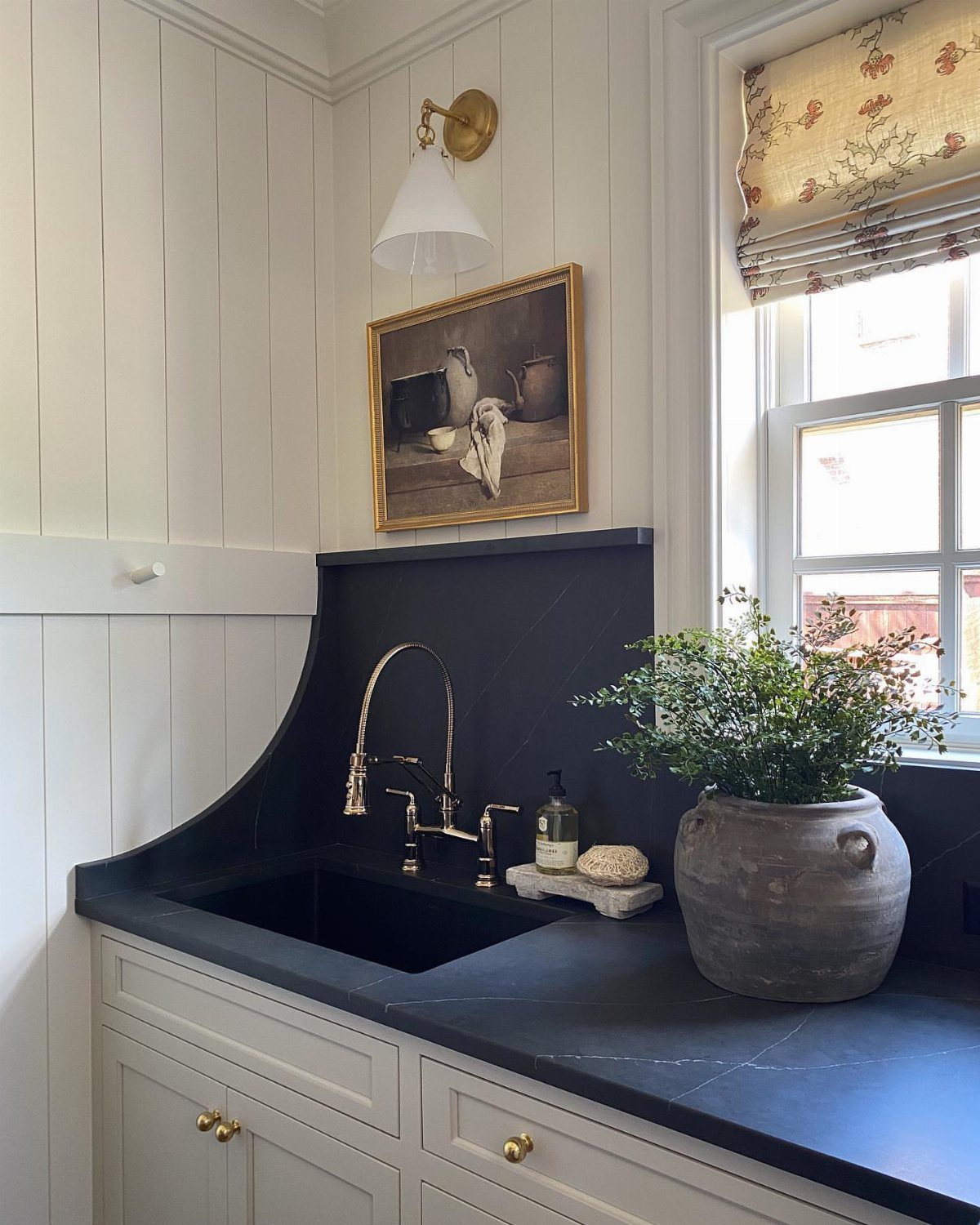 Black undermount sink with gold faucet and a potted plant on dark countertop