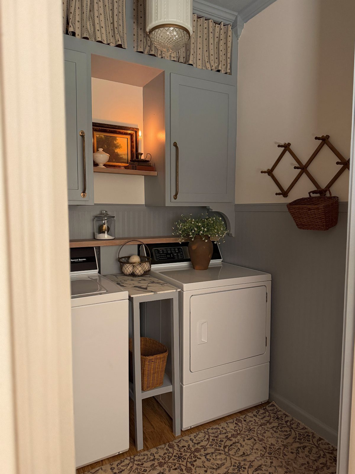 Laundry room with white machines, grey cabinets, a potted plant, and framed artwork.