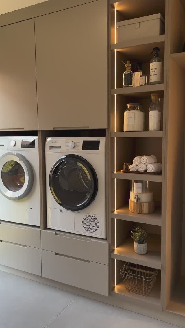 White washing machines integrated into beige cabinetry with an organized open shelving unit.