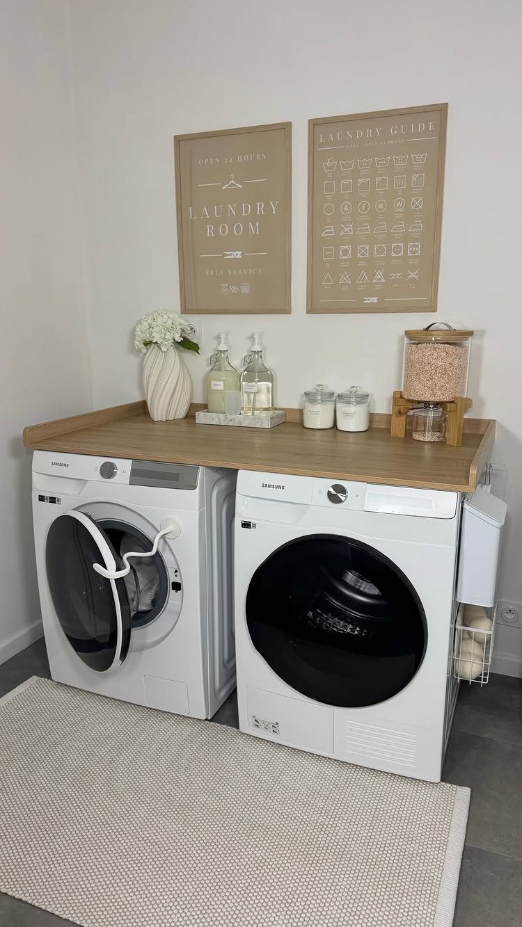 White laundry machines with a wooden countertop and framed laundry art on wall