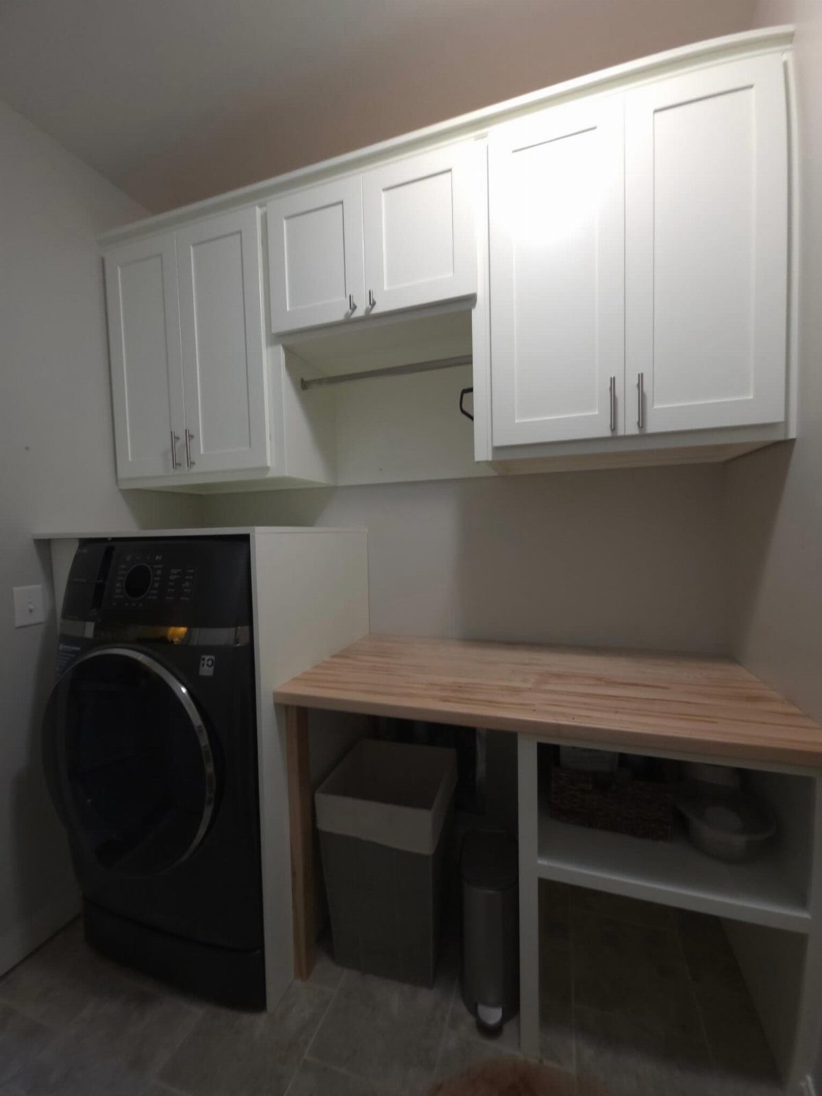 Wooden folding countertop next to a dark grey washing machine with white cabinets.