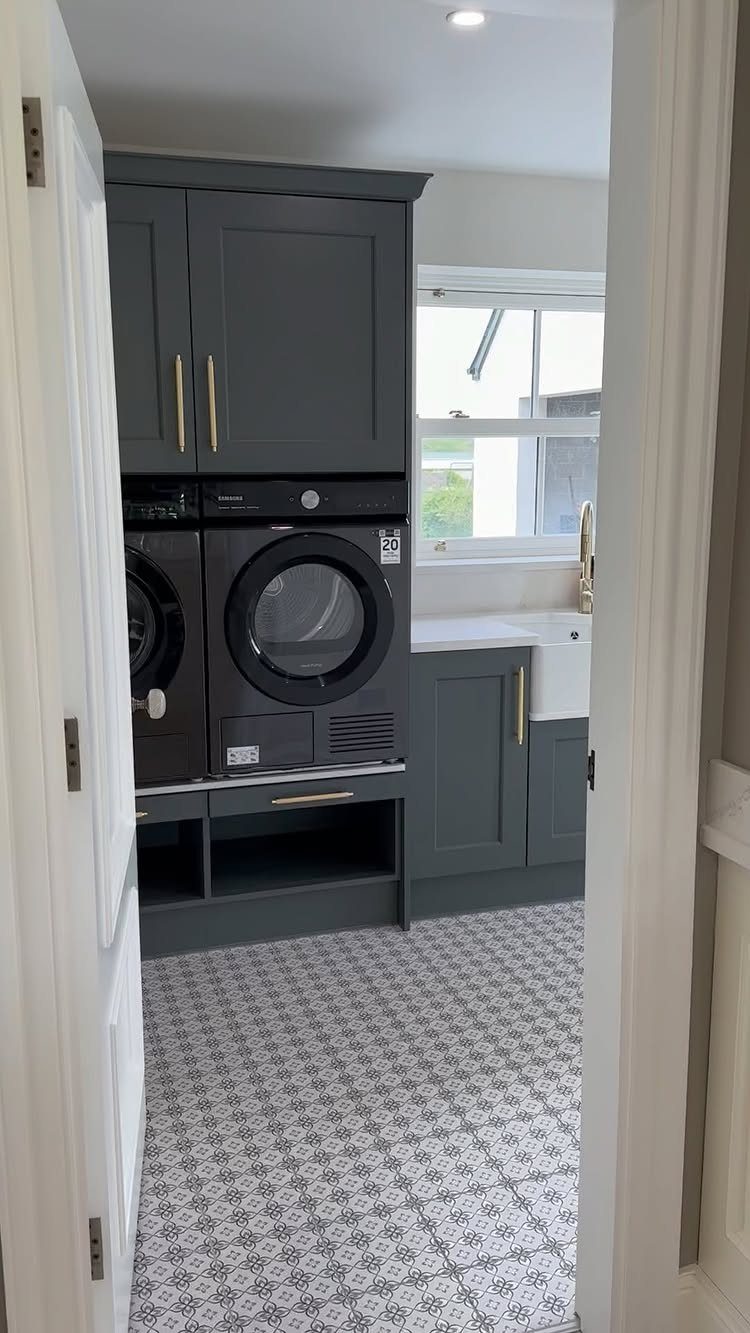 Dark grey laundry room cabinets with gold pulls and patterned floor tiles.