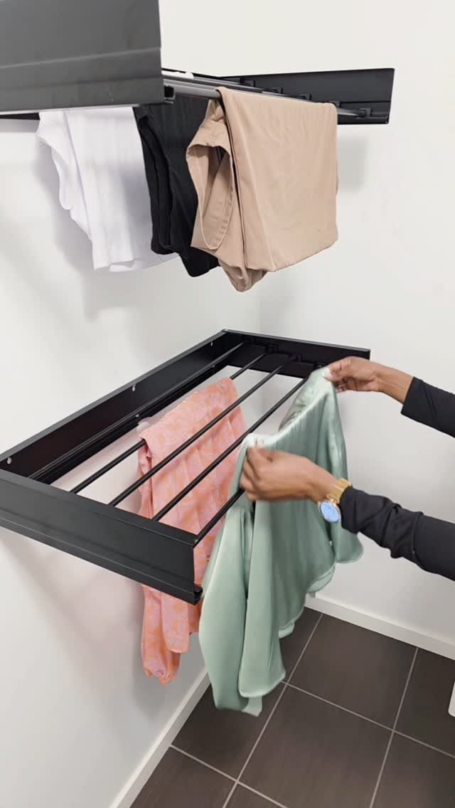 Black wall-mounted drying racks with clothes hanging in a modern laundry area.