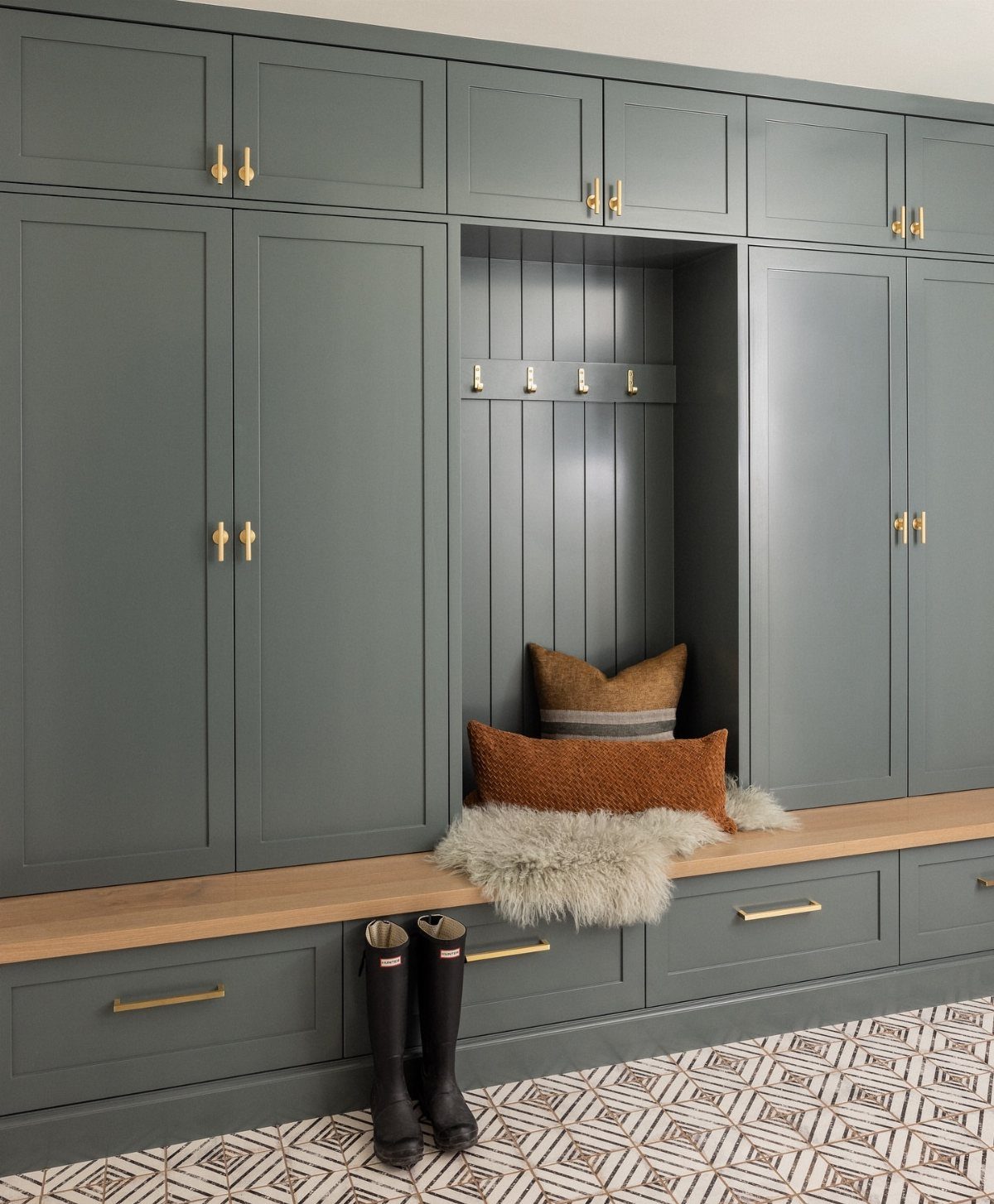 Grey-green built-in mudroom cabinets with a central wooden bench and gold hardware.
