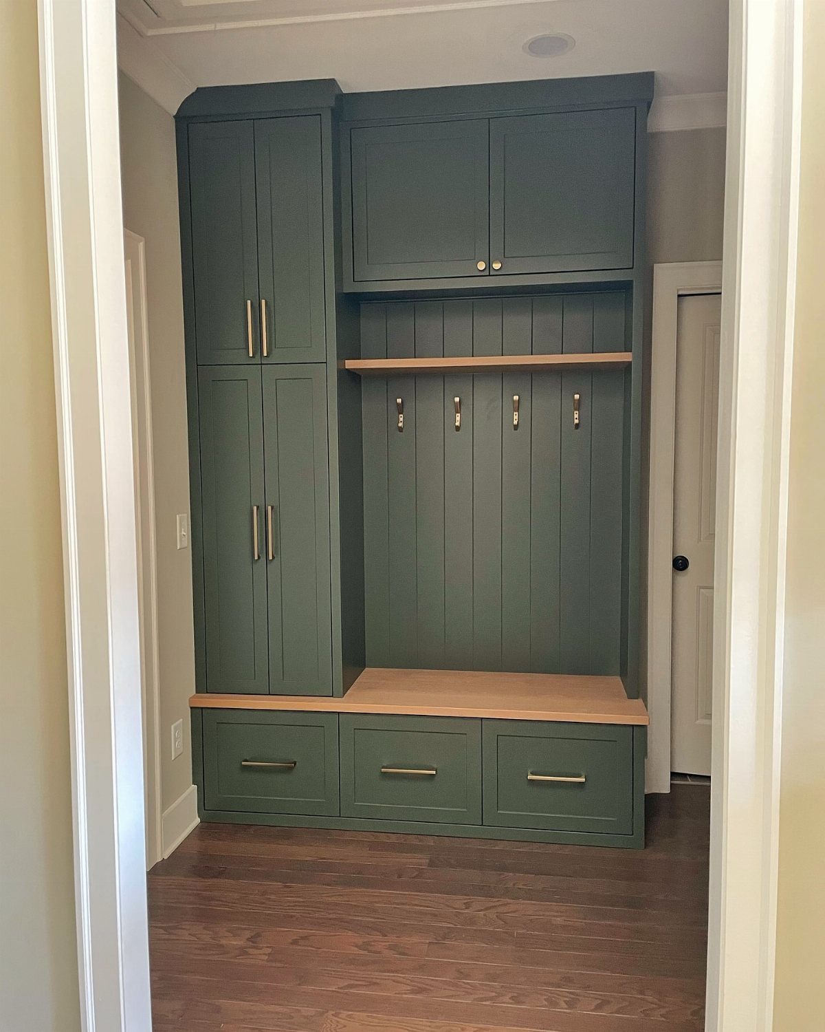 Green built-in mudroom unit with wooden bench, hooks, shelves, and storage cabinets.
