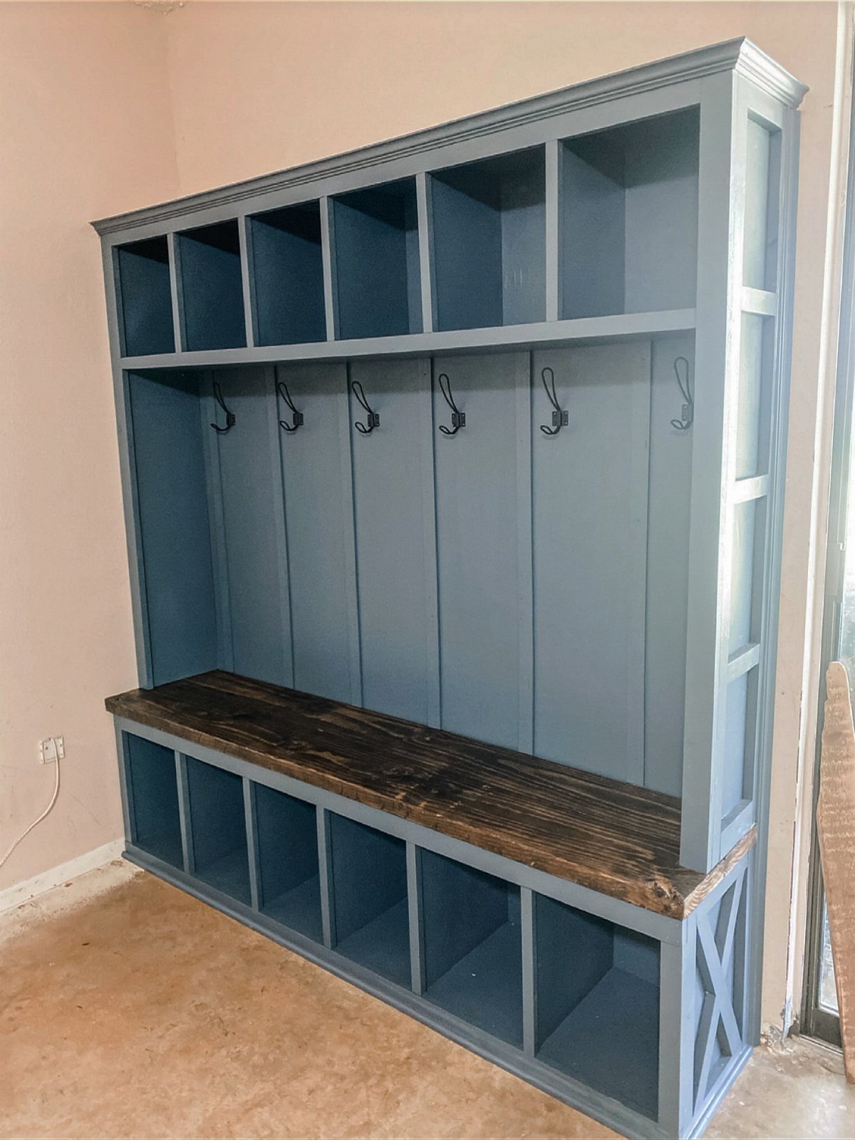 Blue mudroom unit with a dark wood bench, storage cubbies, and black hooks.