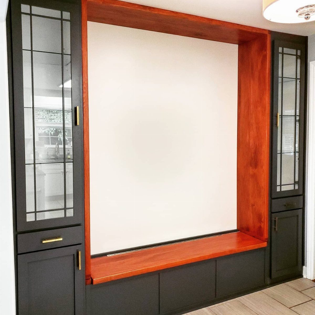 Built-in window seat with dark grey base cabinets and reddish-brown wood top.