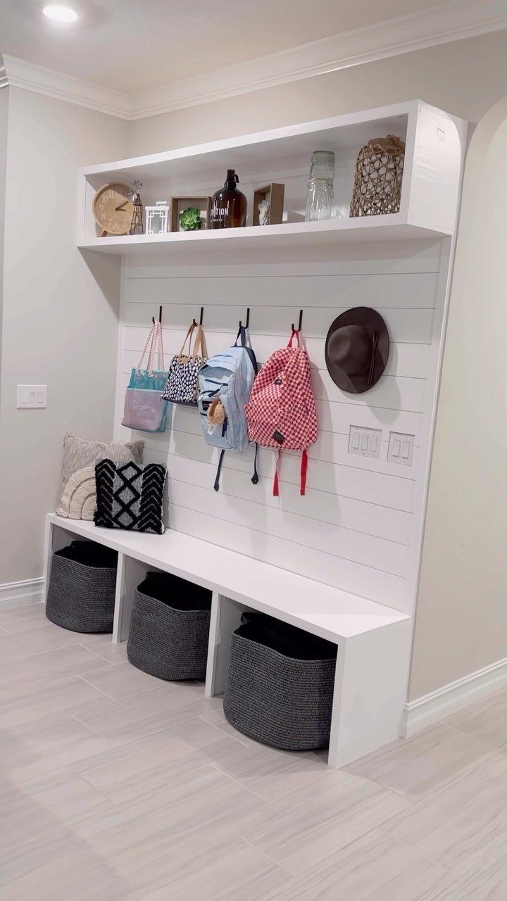 White mudroom entryway unit with a bench, storage baskets, and hooks for bags.