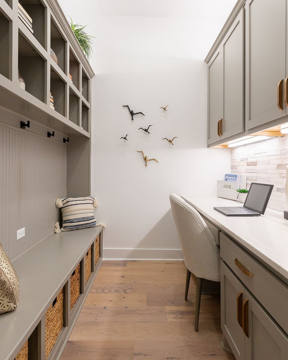Grey mudroom bench with woven basket cubbies, wall hooks, and overhead open shelving.