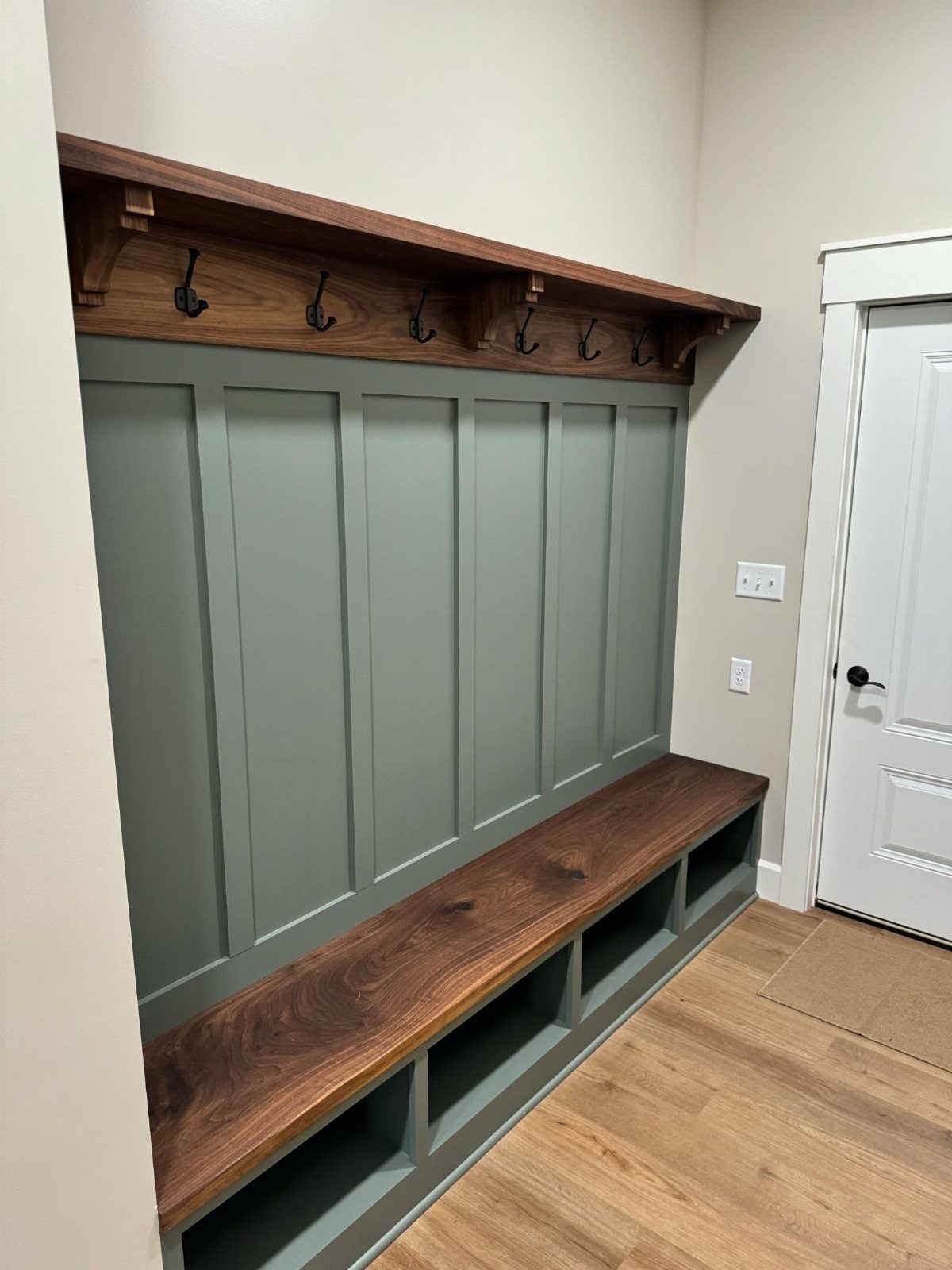 Built-in mudroom bench with sage green paneling and open shoe shelves below.