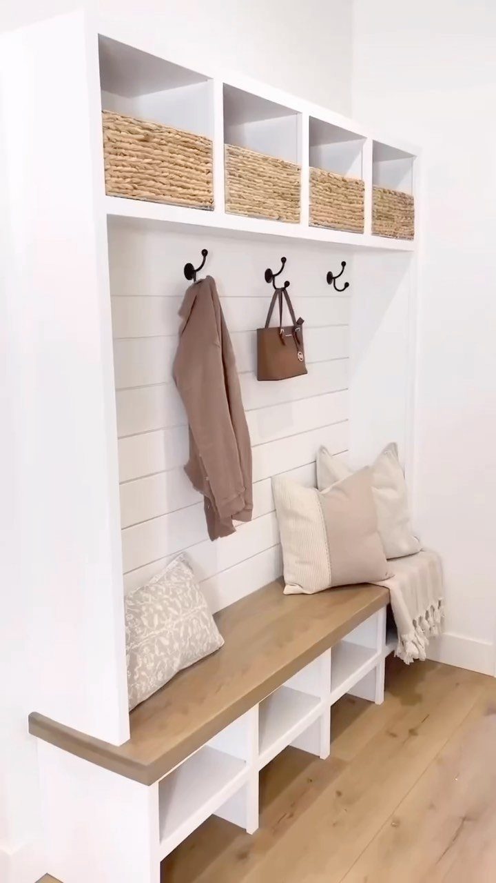 White mudroom unit with wooden bench, woven baskets, and hooks for storage.