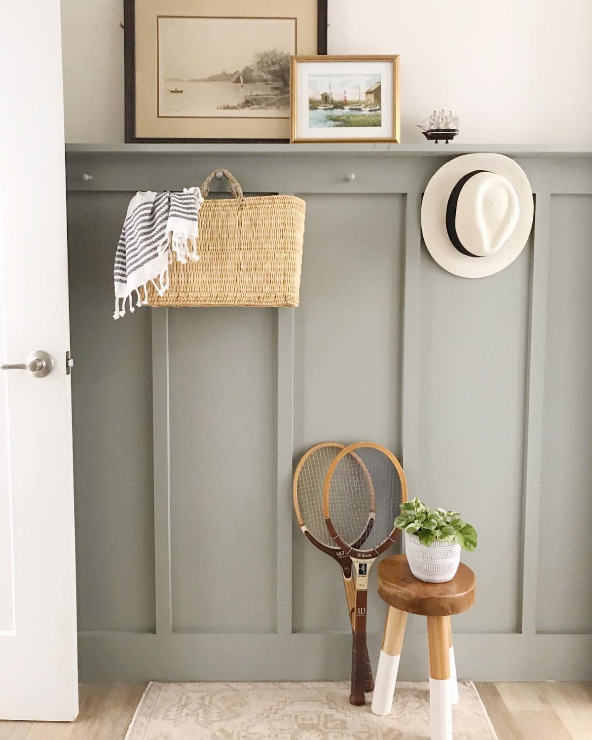 Grey wainscoted accent wall with a ledge, hanging straw bag, and vintage tennis rackets.