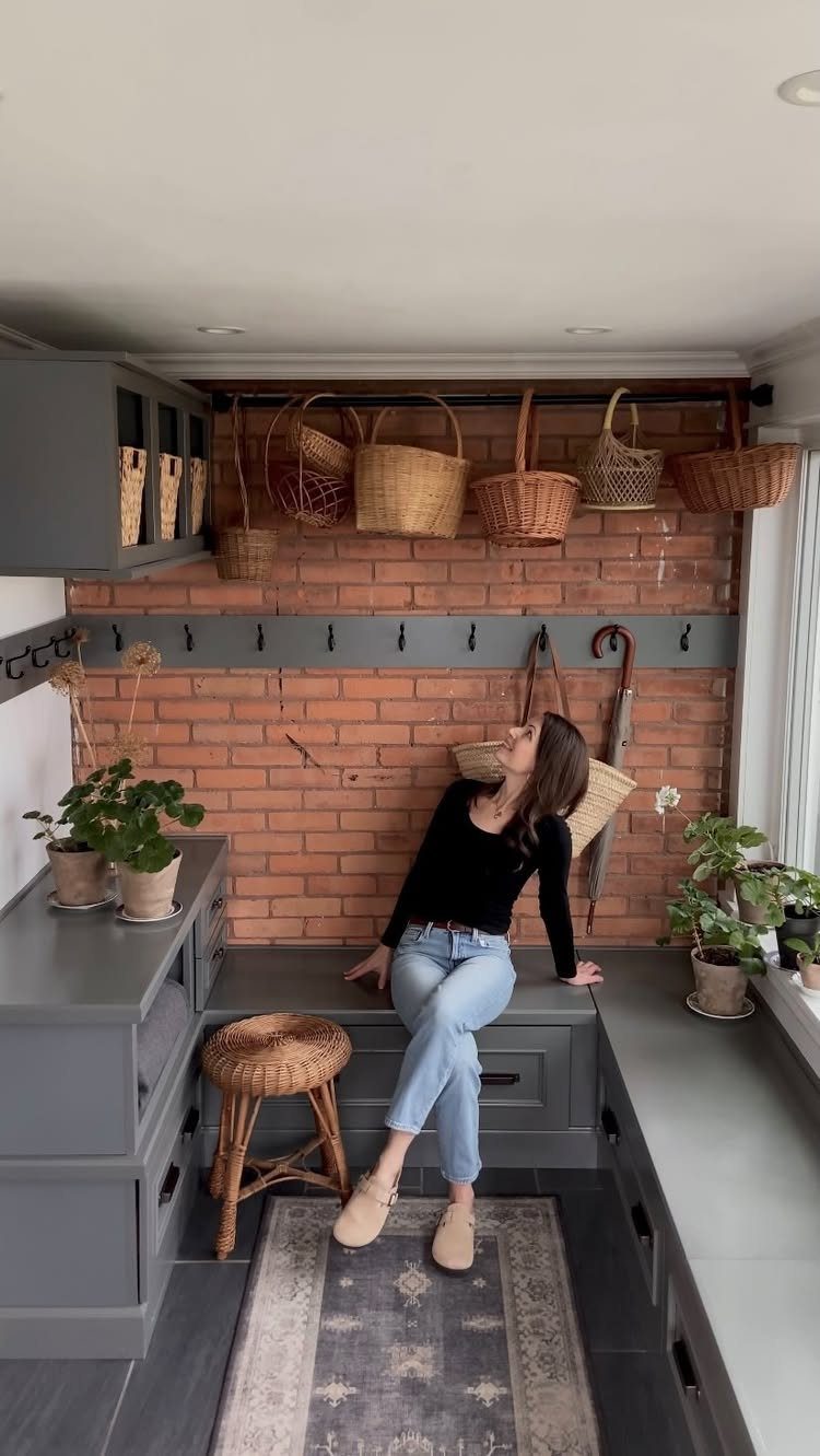 Woven baskets hanging on a rail above a grey mudroom bench and brick wall.