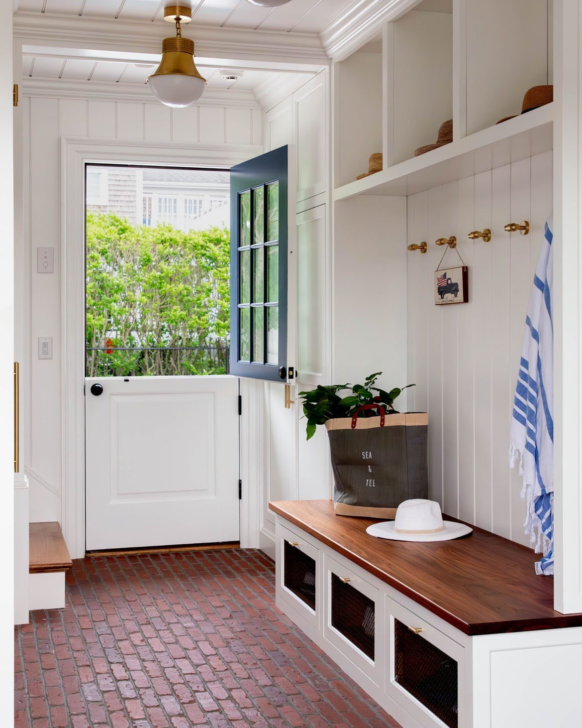 White Dutch door with top half open in a mudroom with brick floors.