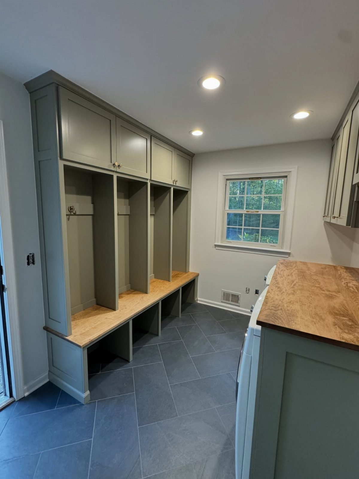 Grey built-in mudroom lockers with a wooden bench and overhead storage cabinets.