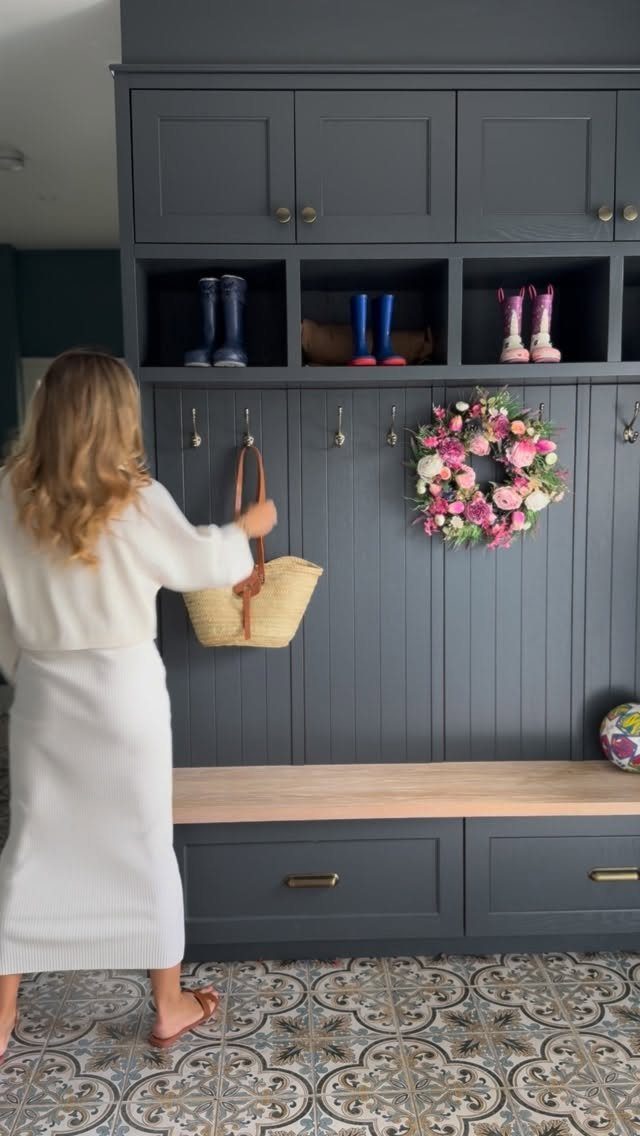 Woman hanging a bag on a dark grey built-in mudroom storage unit with bench.