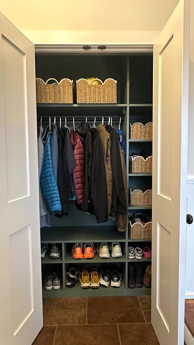 Dark grey mudroom closet with upper storage cubbies containing wicker baskets and shoe storage.
