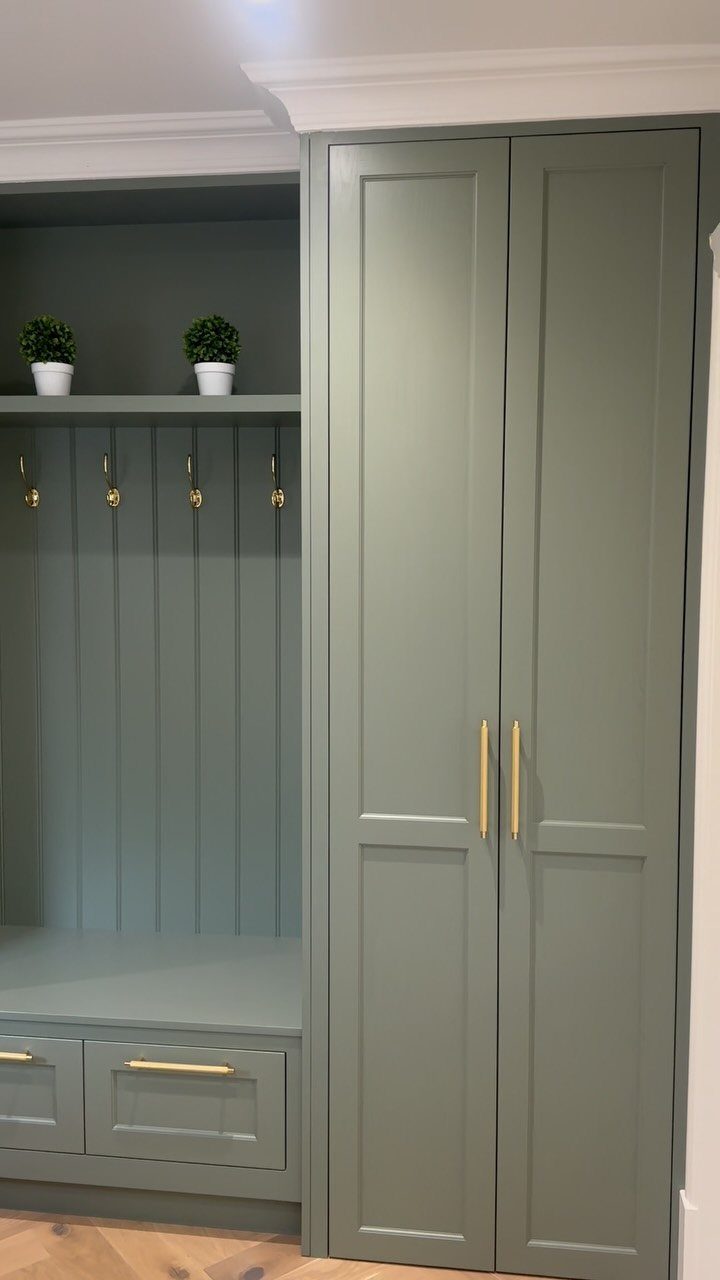 Sage green built-in mudroom cabinets with gold hardware, a bench, and wall hooks.