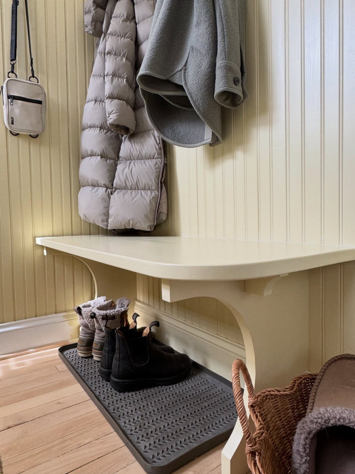 Small mudroom corner with white built-in bench, hanging coats, and boot tray.