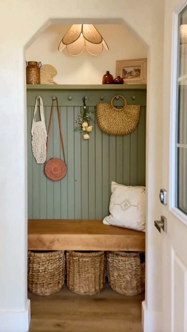 Sage green mudroom nook with wooden bench and woven storage baskets underneath.