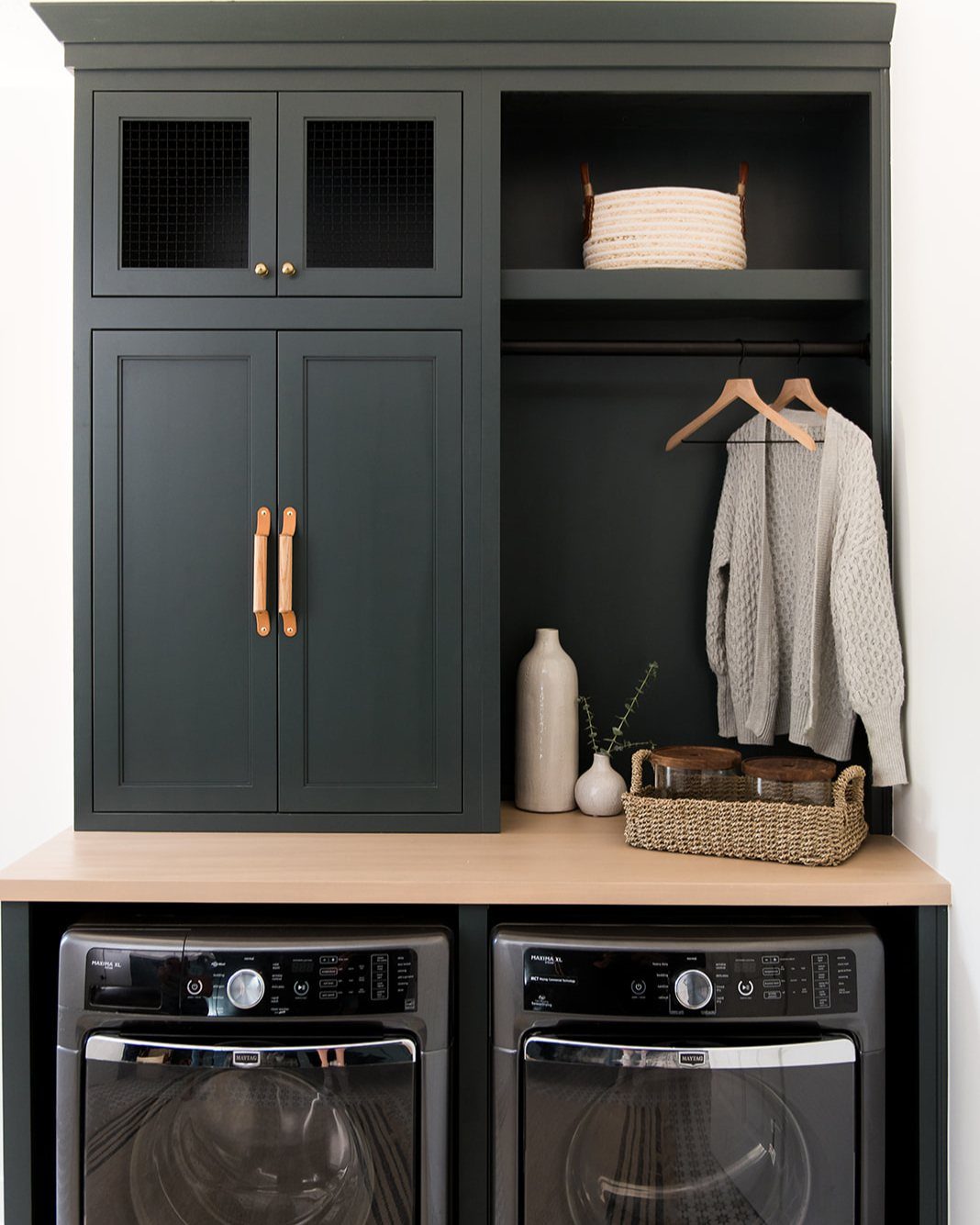 Dark green built-in mudroom storage unit positioned above two front-loading laundry machines.