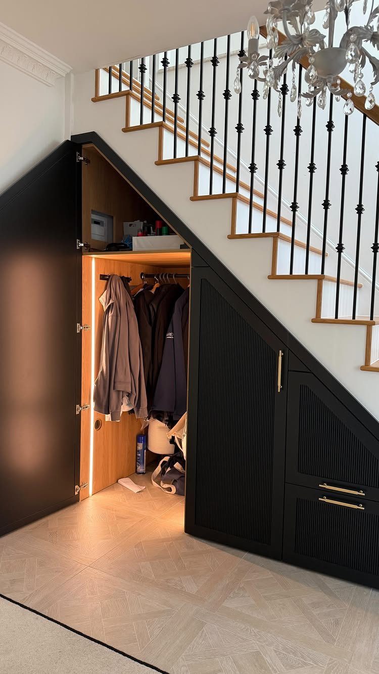 Black built-in storage closet under a staircase containing hanging coats and shelves.