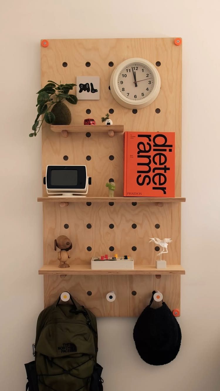 Plywood pegboard with shelves and hooks holding a backpack and hat on white wall