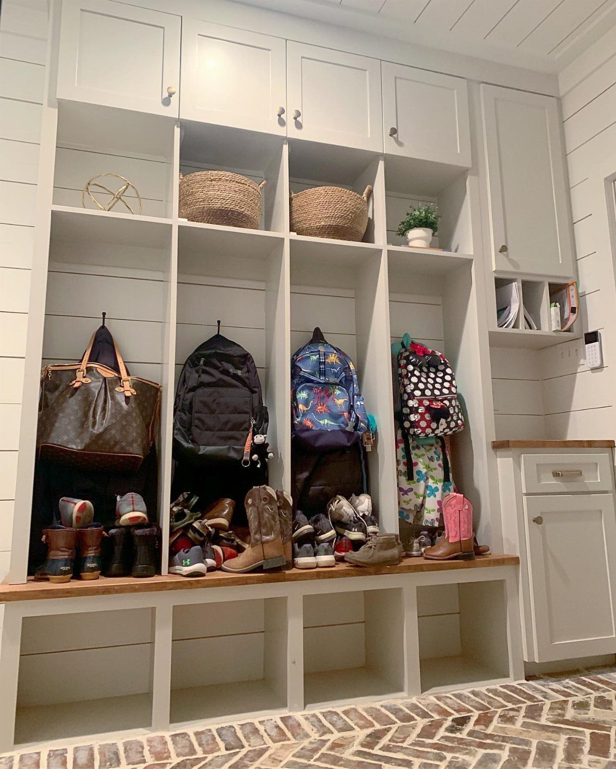White built-in mudroom unit with vertical cubbies, hooks, and a wooden storage bench.