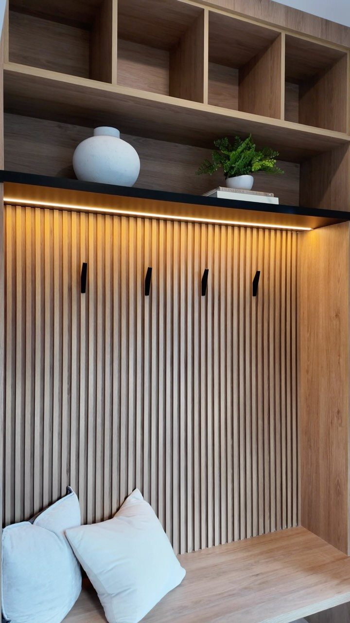Light-wood wall-mounted mudroom unit with slatted paneling, black hooks, and open shelving.