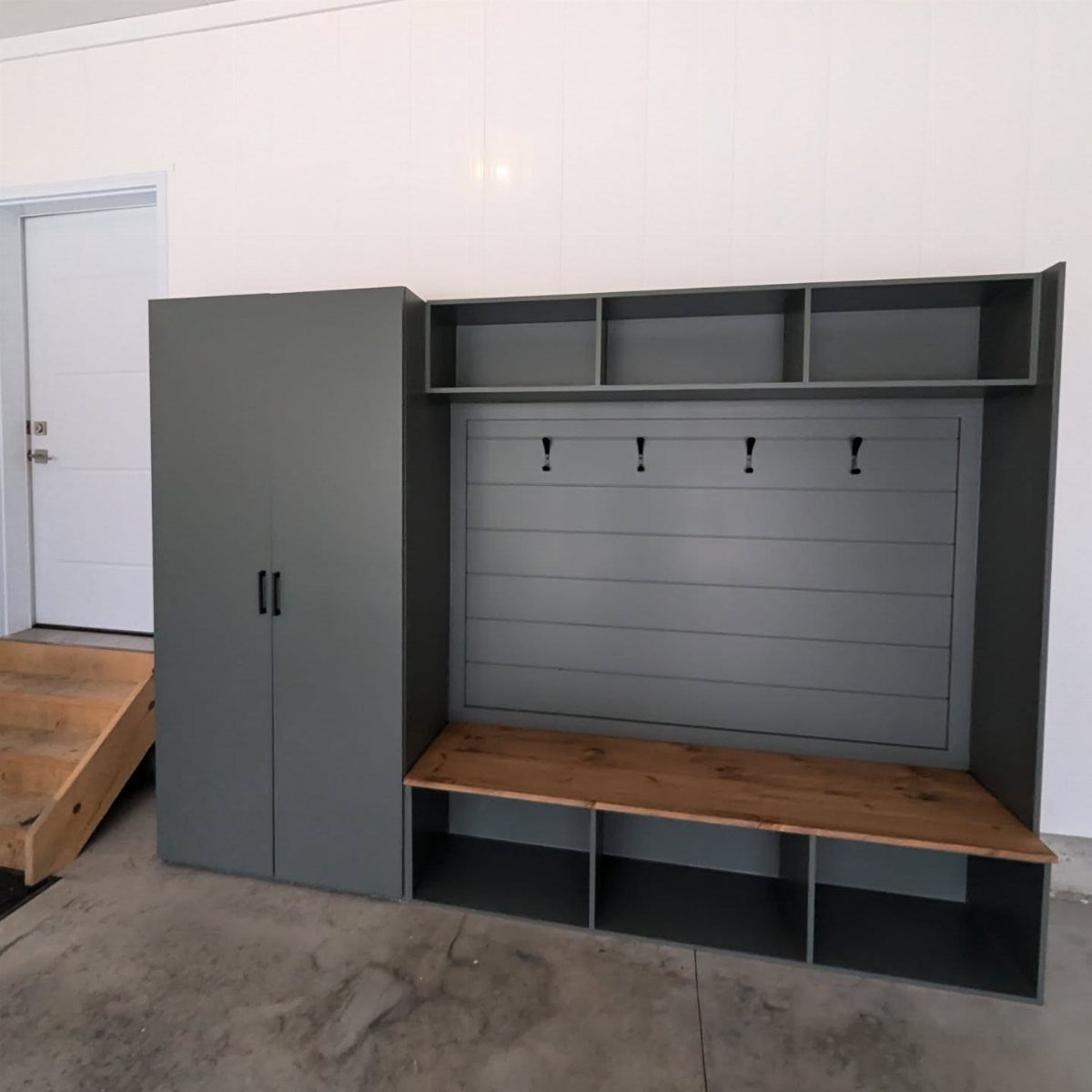 Grey built-in mudroom unit with wooden bench and hooks in a garage setting.