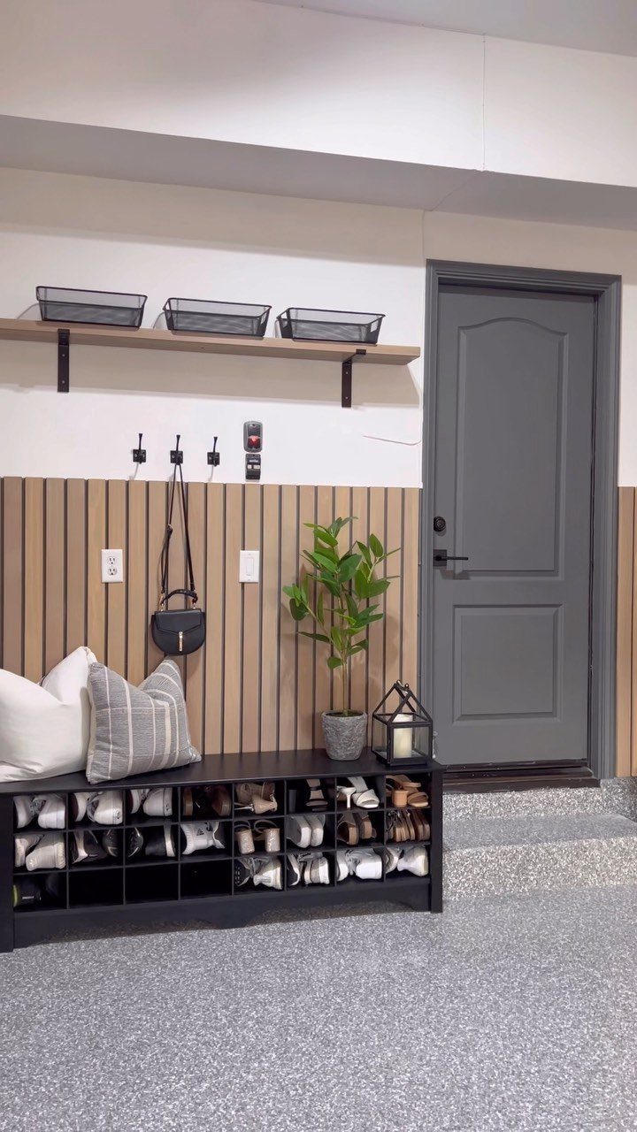Black shoe storage bench with pillows against a wood-slat wall in a mudroom.