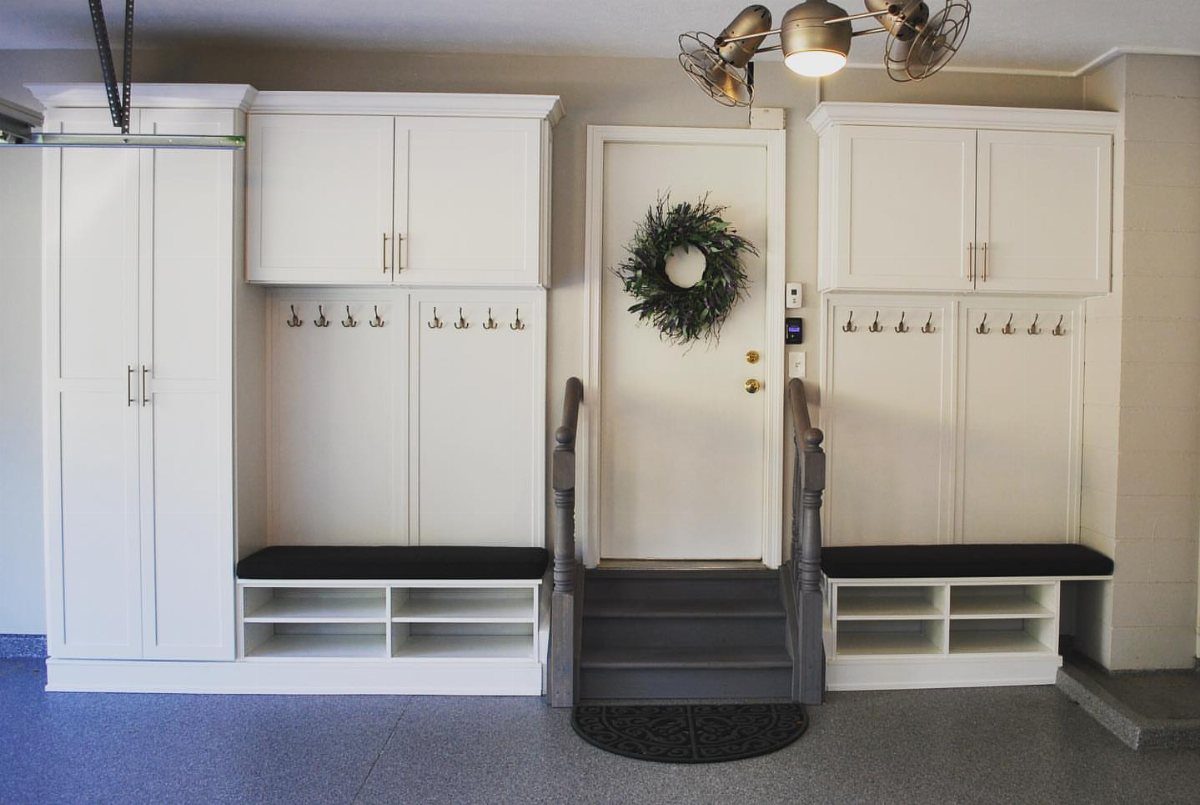 White built-in mudroom cabinetry with benches and hooks next to a garage entry door.