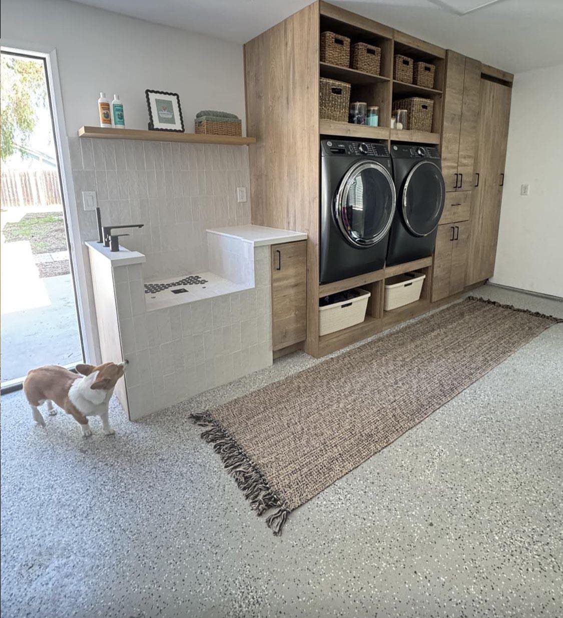 White tiled pet washing station next to wooden laundry cabinets in a garage.