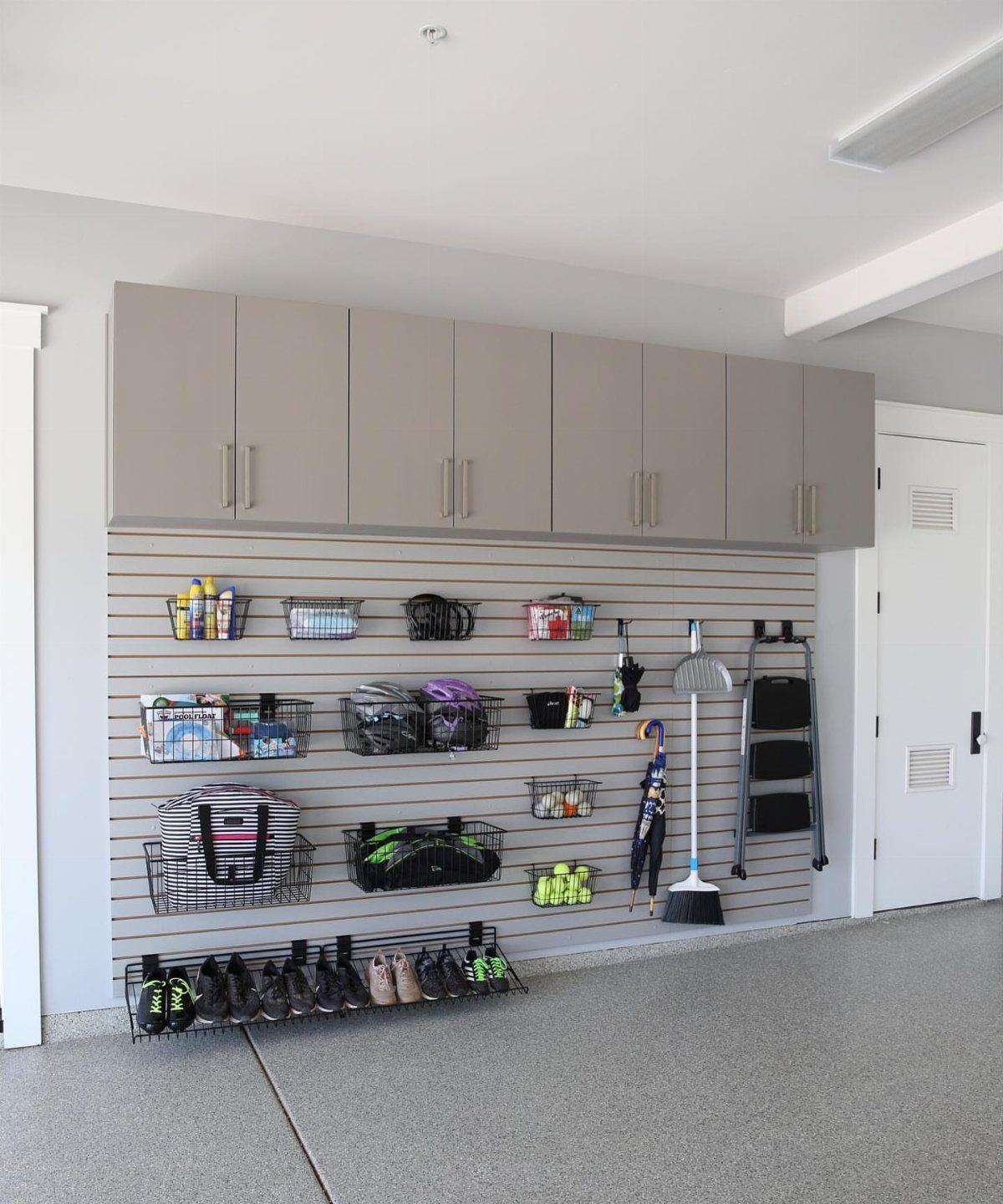 Slatwall storage system in a garage with baskets, broom, and grey cabinets above.
