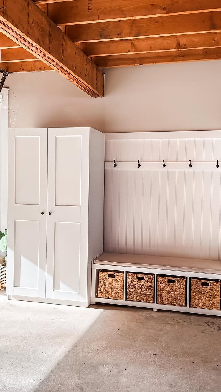 White mudroom storage with a tall cabinet, wall hooks, and bench with baskets.