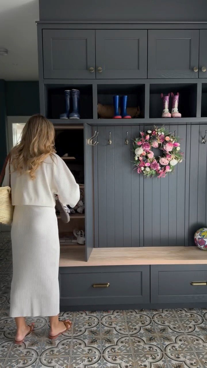Woman standing by a dark grey built-in mudroom unit with boots and bench.