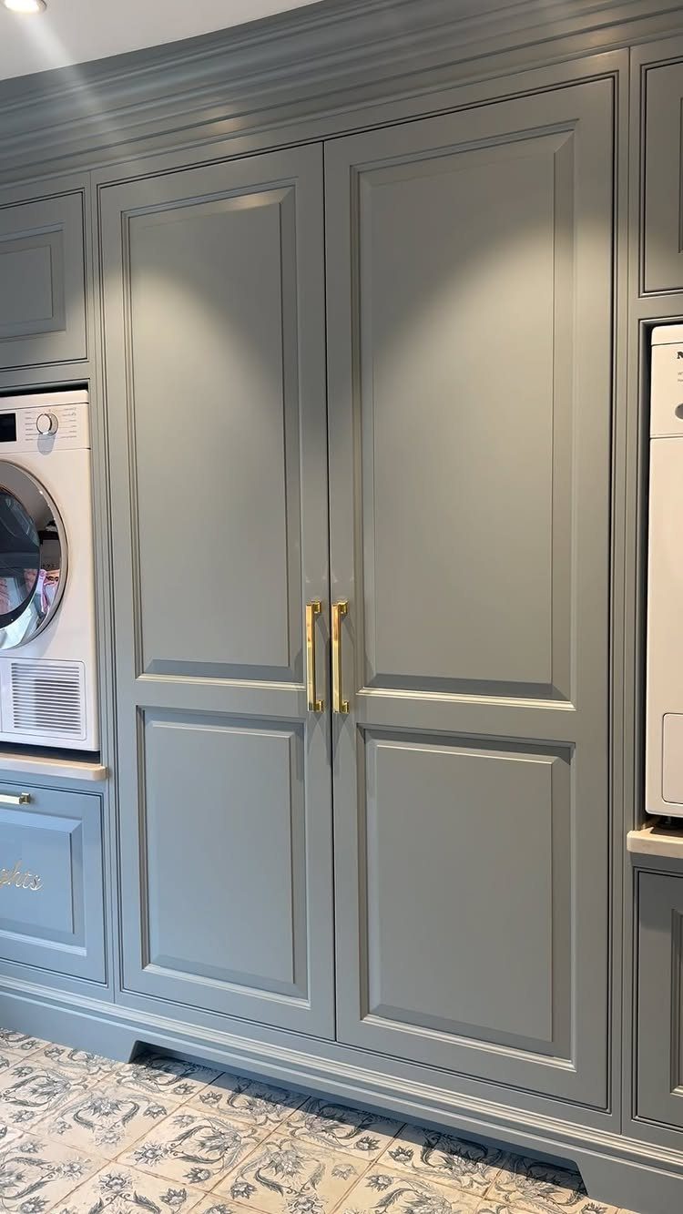 Grey custom cabinetry with gold handles and a washing machine on patterned tiles.
