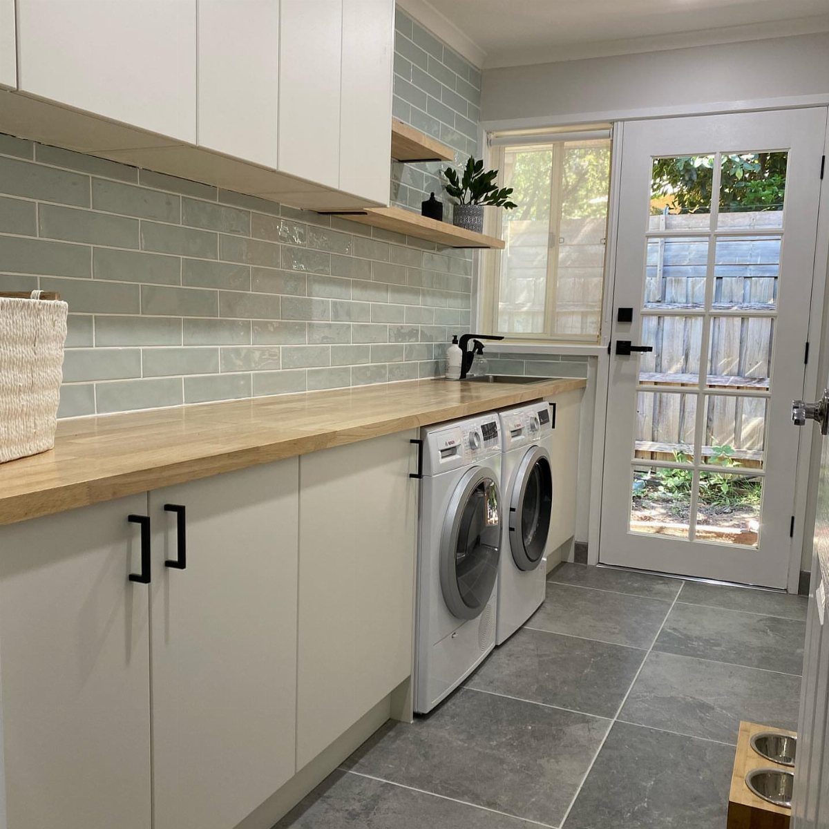 Light blue subway tile backsplash in a modern laundry room with white cabinetry.
