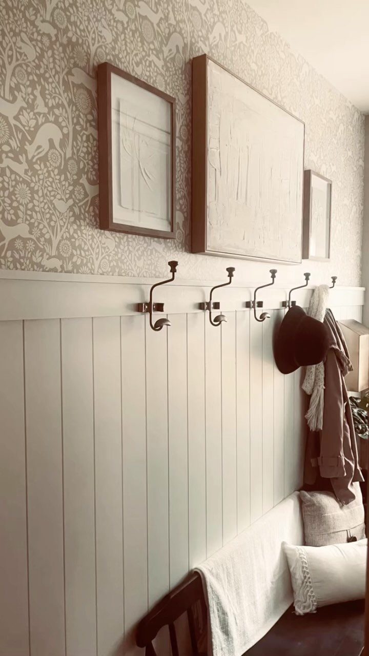 White board and batten wall panel with black hooks and patterned wallpaper above.