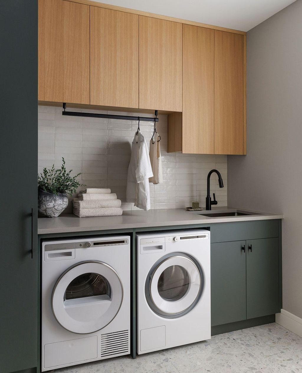 White washer and dryer under a grey countertop with light wood upper cabinets.
