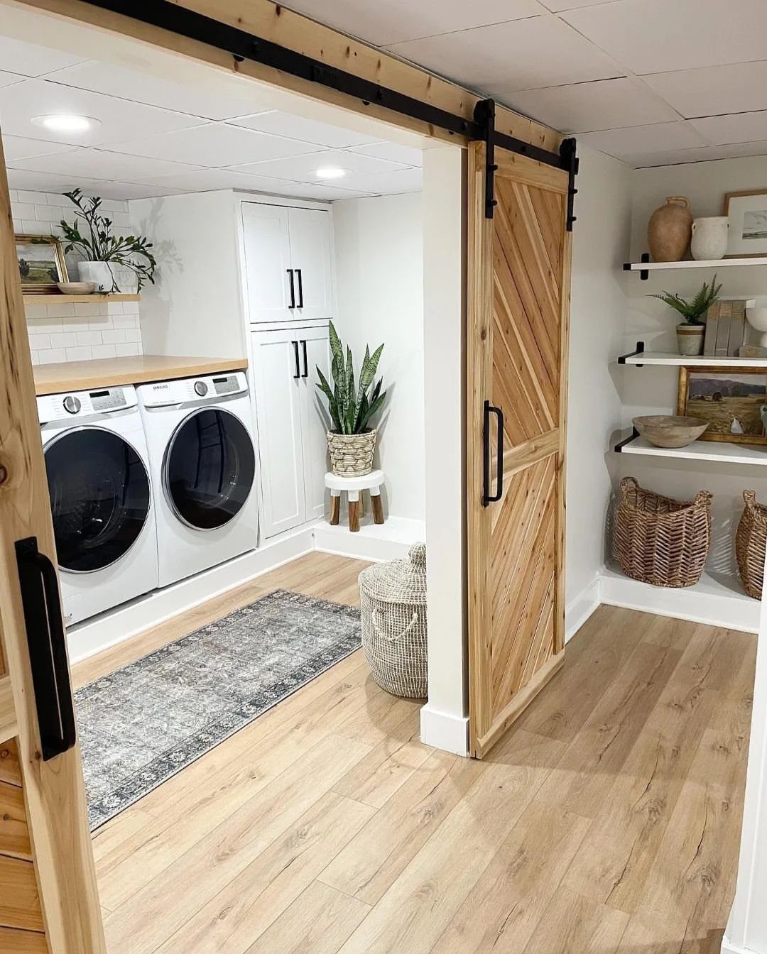 Wooden sliding barn door opening into a bright laundry room with white appliances.