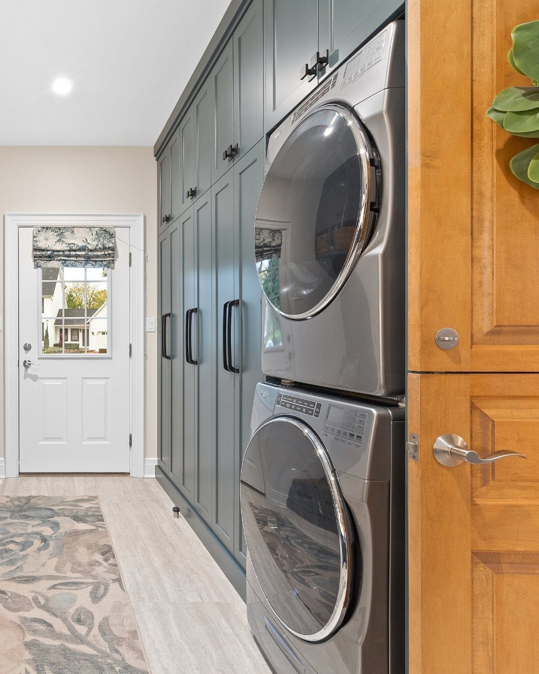 Stacked grey washer and dryer next to grey mudroom lockers and a white door.