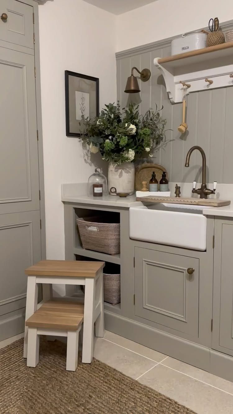 White farmhouse utility sink with bronze faucet and grey cabinetry in a laundry room.