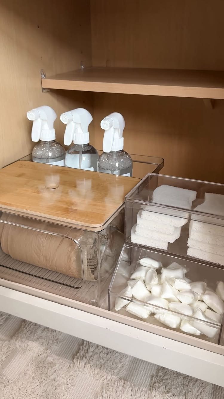 Clear acrylic storage bins filled with white cleaning supplies on a white shelf.