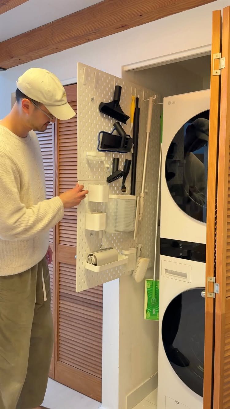 Man organizing cleaning tools on a white wall-mounted pegboard in a laundry room.