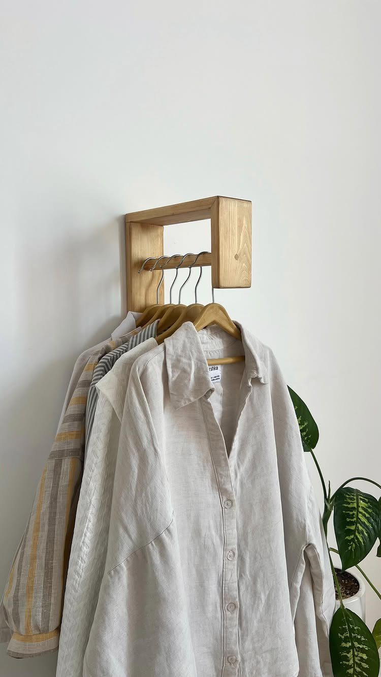Wooden wall rack holding linen shirts on hangers against a white wall