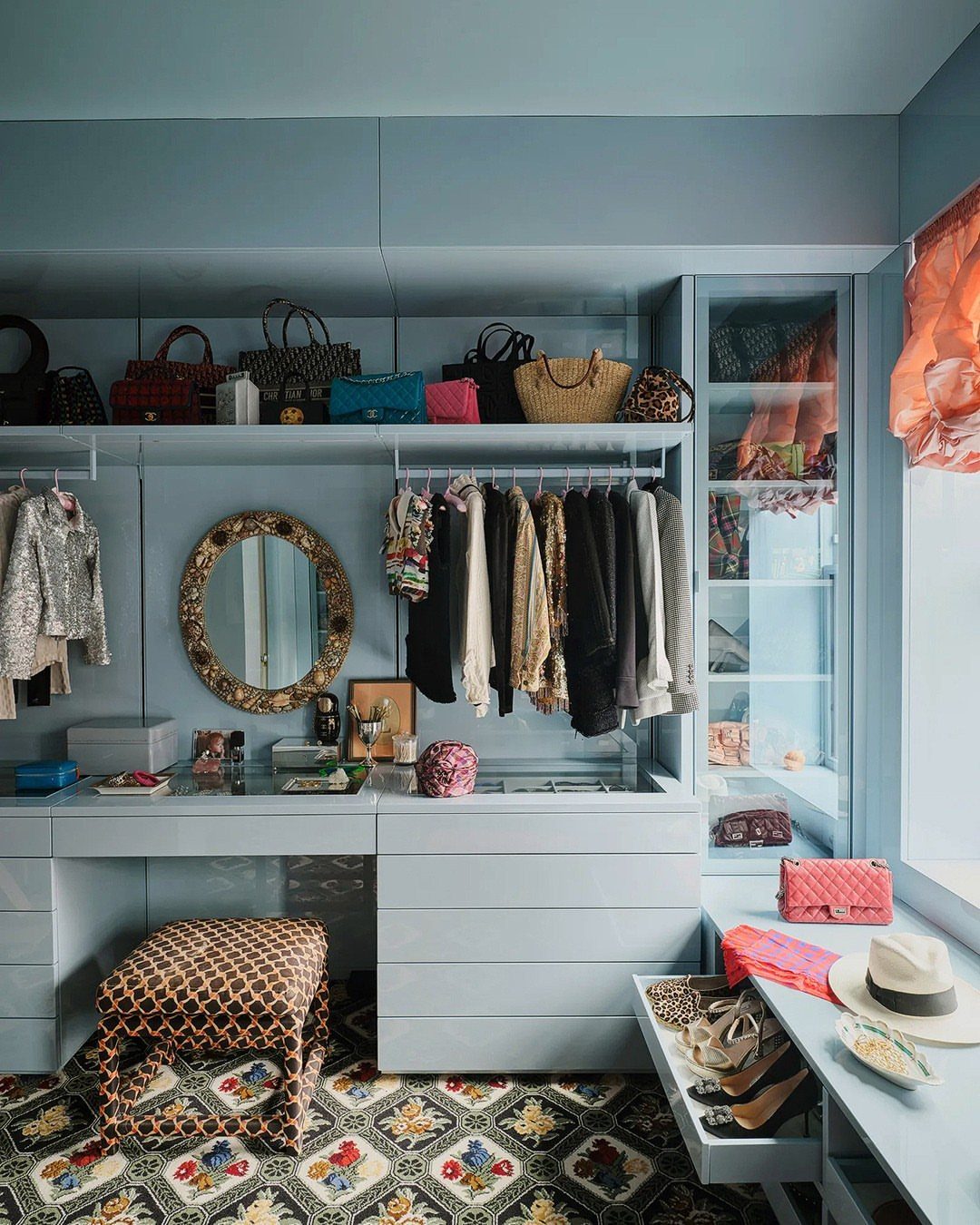 Light blue walk-in closet with handbags displayed on a high shelf and vanity.