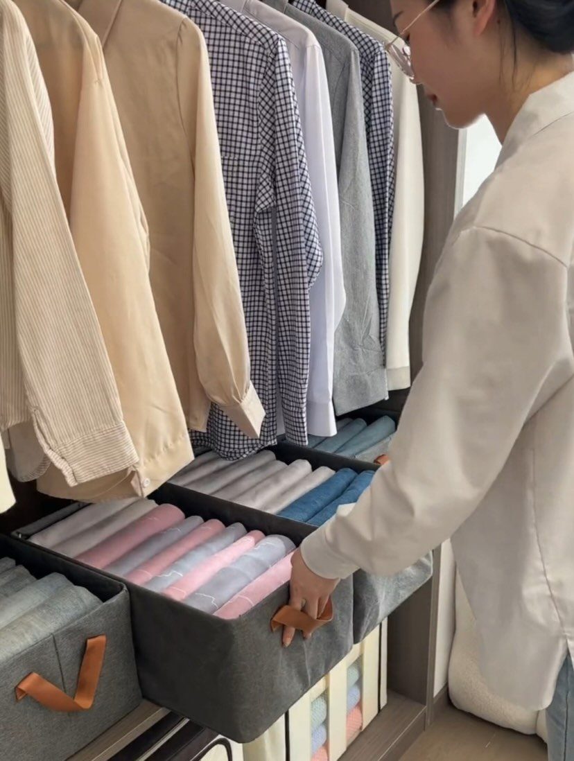 Person pulling a grey fabric bin of folded clothes from a closet shelf
