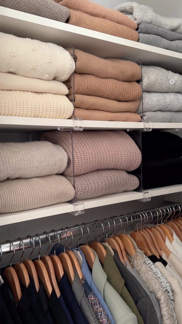 Folded neutral-toned sweaters on white closet shelves with clear acrylic dividers.